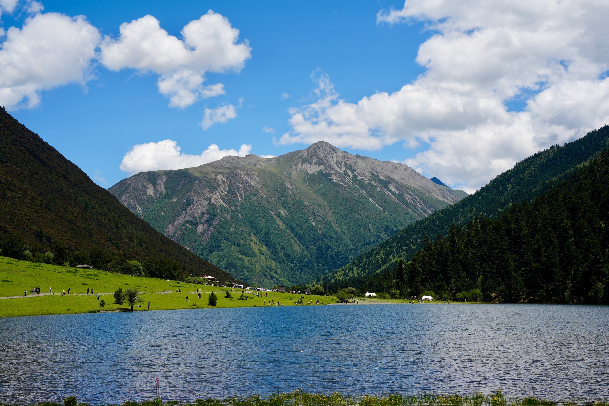 A blue alpine lake below green mountains and bright summer clouds near Shangri-La