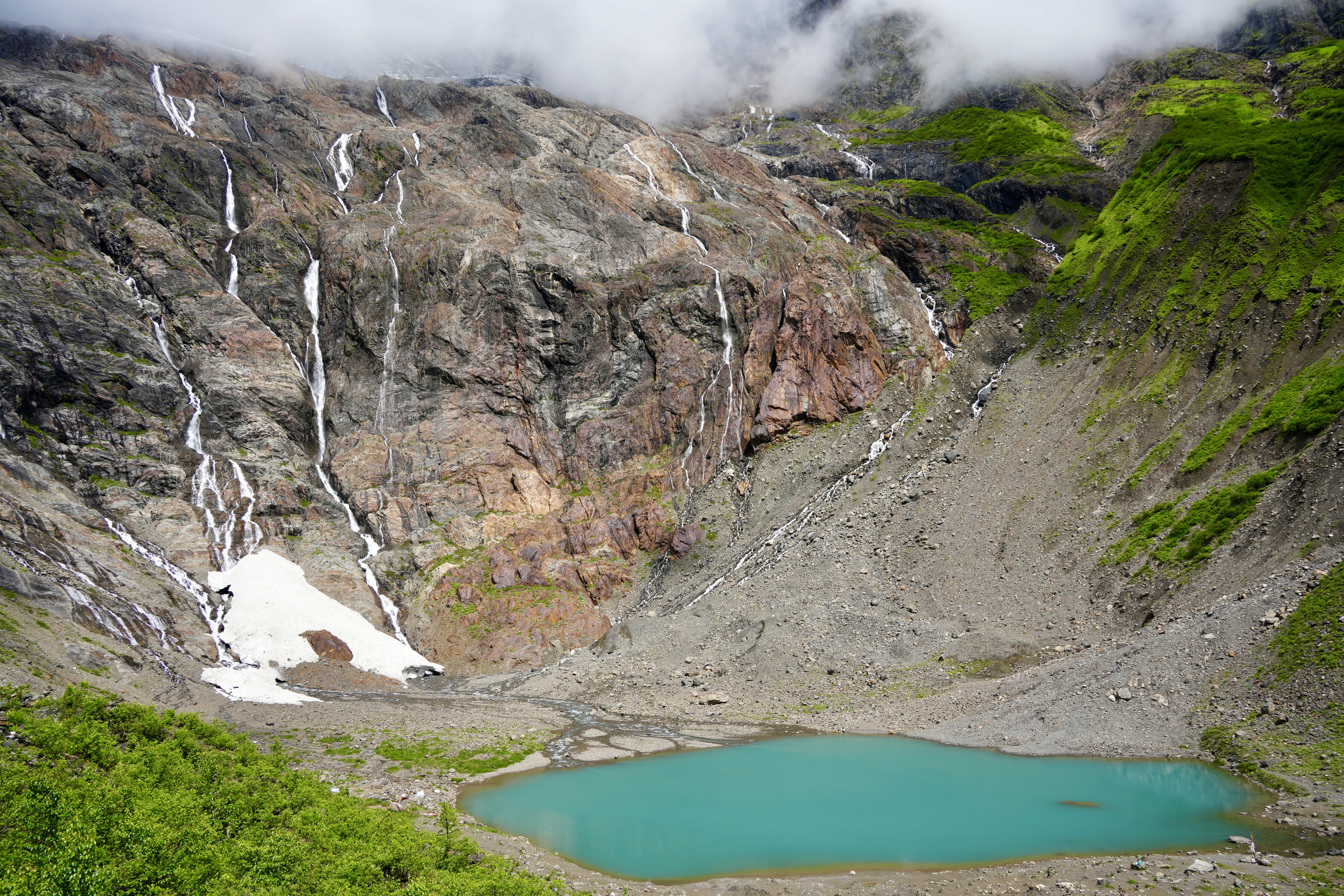 Turquoise Ice Lake below waterfalls and cloud-covered rock walls near Yubeng